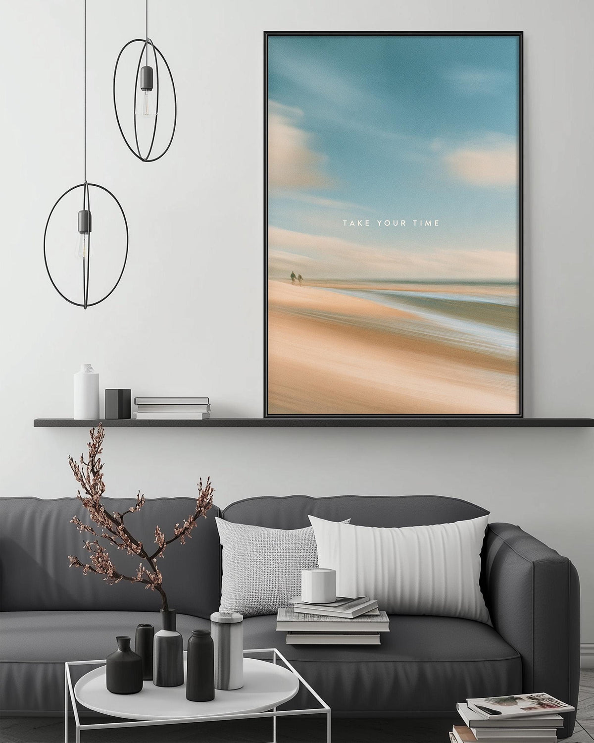 a modern living room with a gray sofa, a coffee table, and a large framed picture of a beach scene above it. The room has a minimalist and stylish design, with a pendant light fixture hanging above the sofa and a shelf below the picture.