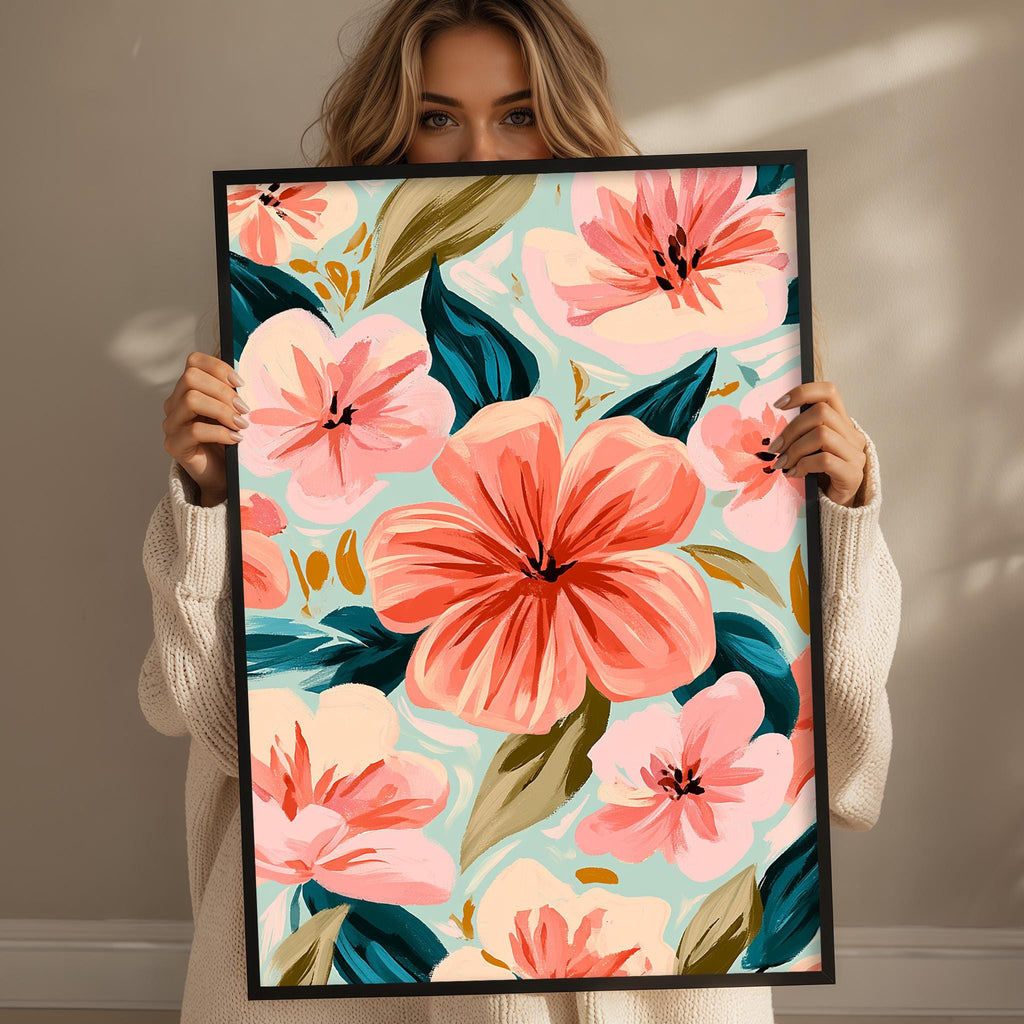 A woman is holding up a framed print with a vibrant floral design featuring pink and orange flowers against a light blue background.