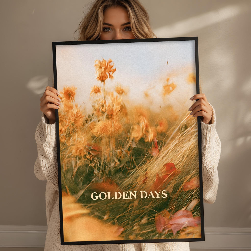 A woman holding a framed print with a vibrant field of flowers and the text "GOLDEN DAYS" on it.