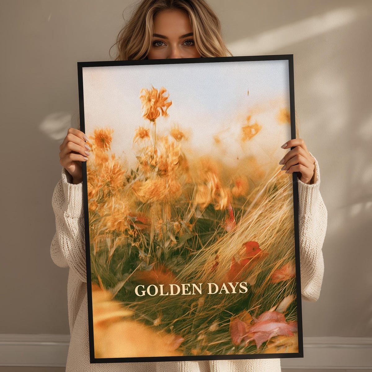 A woman holding a framed print with a vibrant field of flowers and the text "GOLDEN DAYS" on it.
