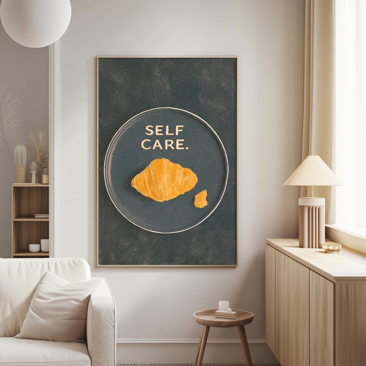 a living room with a large framed poster on the wall that reads "SELF CARE." The poster has an illustration of a croissant on it. The room also includes a white couch, a small table, and a lamp.