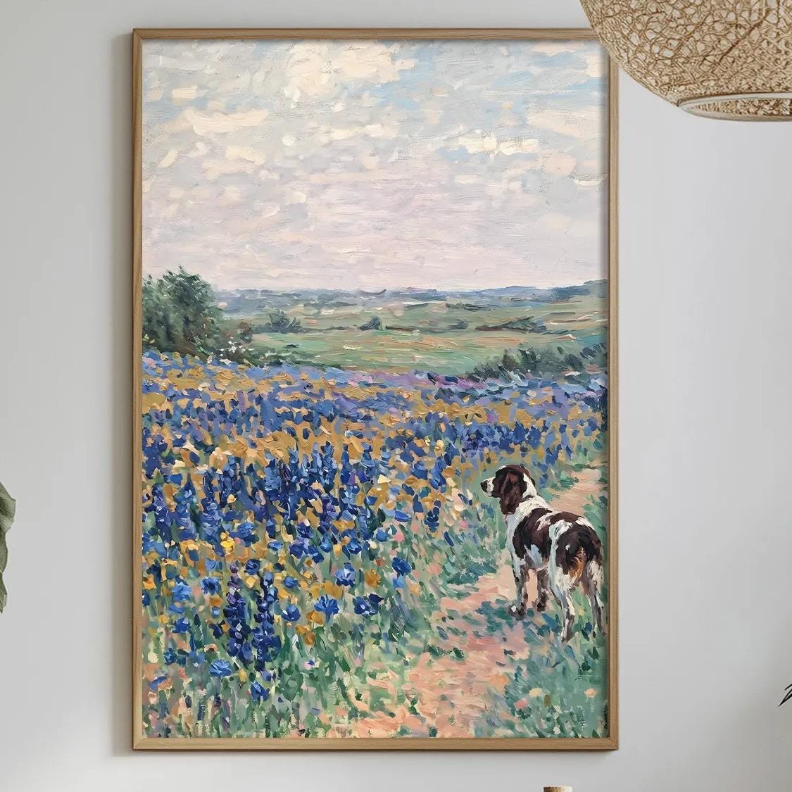 a dining table with a white tablecloth, a bowl of fruit, a bottle, and a vase with flowers. Above the table, there is a framed painting depicting a field of flowers.