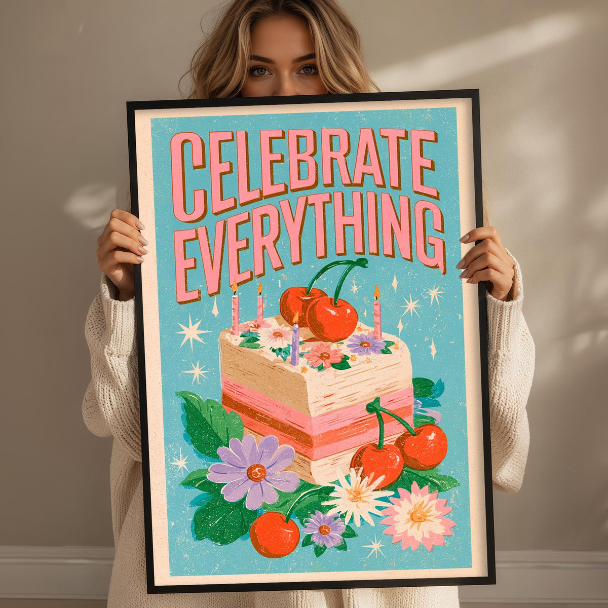 A woman holding a framed poster with a colorful illustration of a cake, flowers, and cherries.