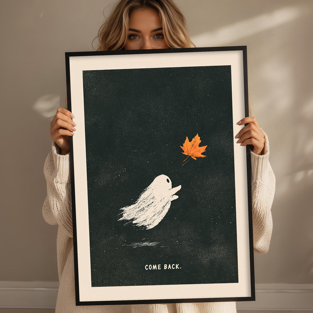 A woman holding a framed poster with a ghost and a leaf, with the text "COME BACK."