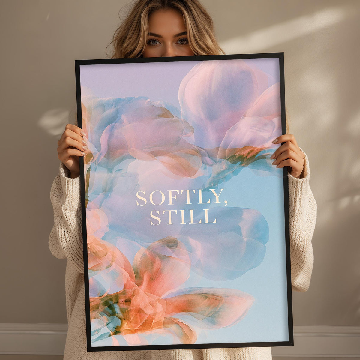 A woman holding a framed poster with a floral design and the text "SOFTLY, STILL" printed on it.