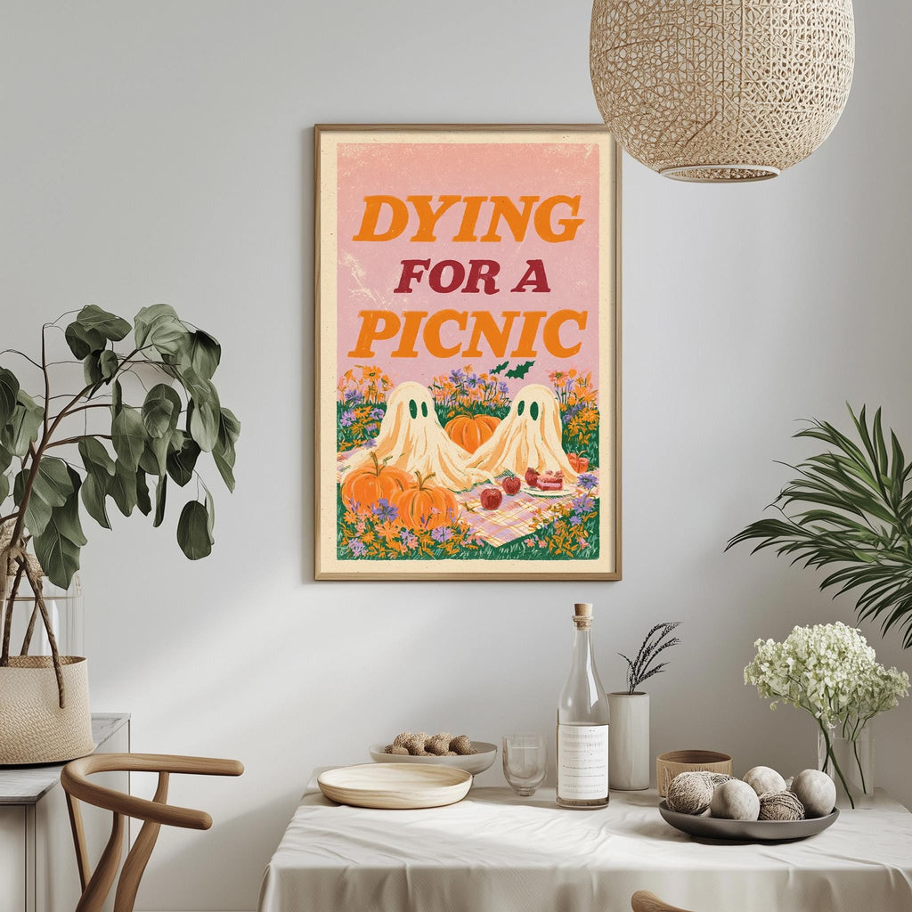 a framed poster with the text " Dying for a Picnic" hanging on a wall above a dining table with various items on it, including a bottle, a bowl, and a vase.