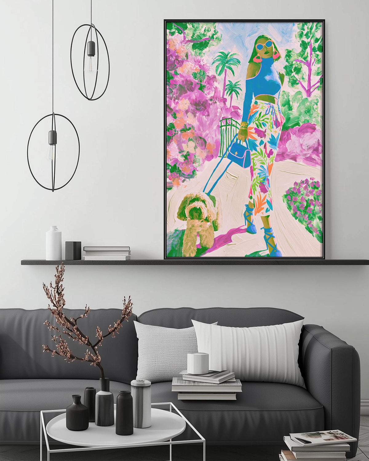a large, colorful painting of a woman walking down a path, surrounded by a vibrant garden scene. The painting is displayed on a wall above a gray couch, which is adorned with various decorative items such as vases, a potted plant, and a stack of books. The overall setting appears to be a cozy and inviting living space.