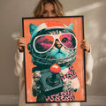 A woman is holding up a framed poster featuring a cat wearing a spacesuit and sunglasses, with a red button in its paw.