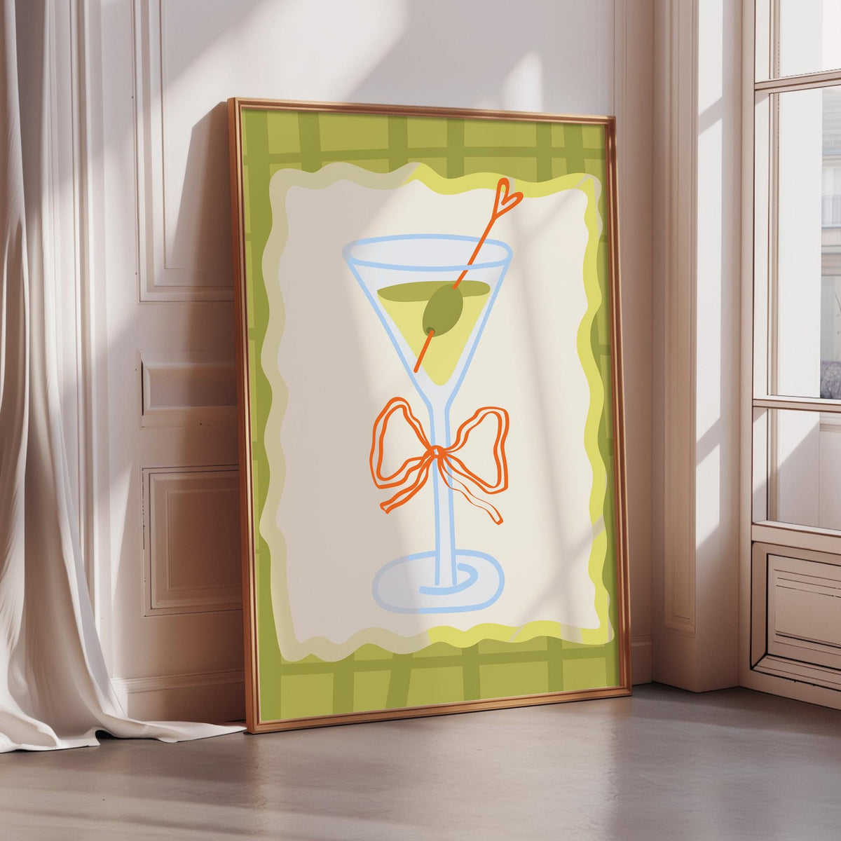 A framed illustration of a martini glass with a green olive garnish is displayed on a wall in a room with a window.