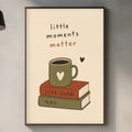 a kitchen counter with various items, including a coffee mug, a book, a cutting board, and a plant. Above the counter, there is a framed poster with the text "little moments matter" and an illustration of a book and a coffee mug.
