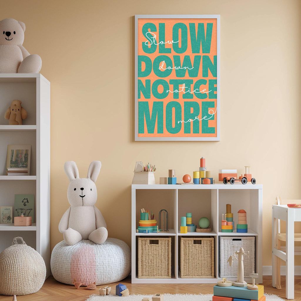 A child's bedroom with a stuffed rabbit, a bookshelf, and a toy storage unit. The wall has a framed poster with the text "Slow down, notice more" in orange and green.