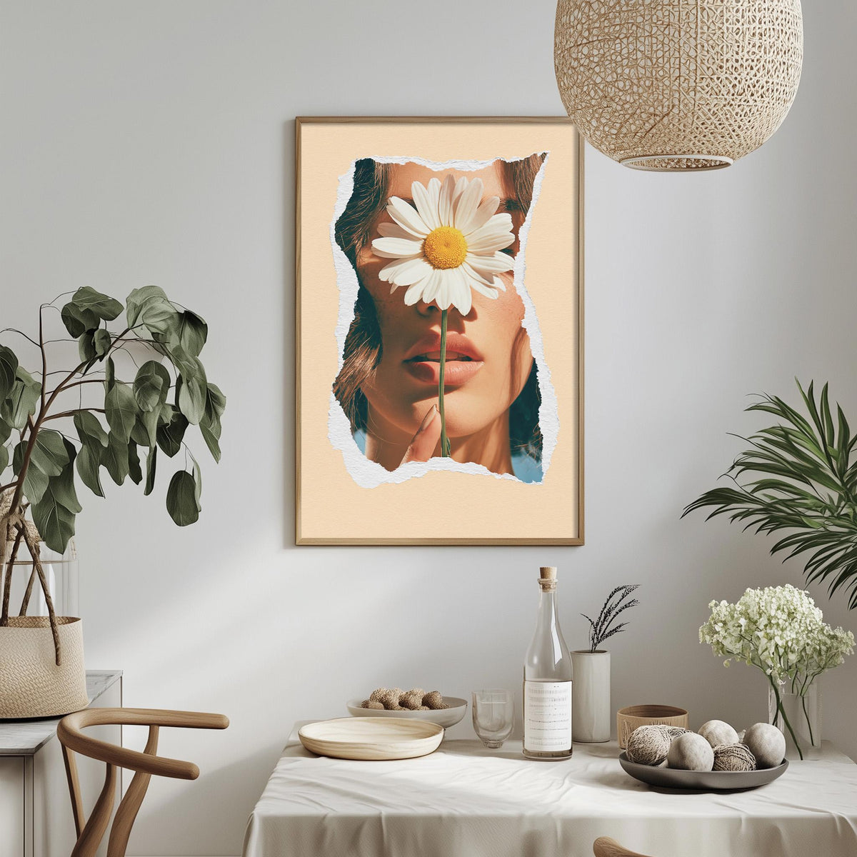 a framed collage of a woman's face with a large white flower covering her eyes, set against a light peach background. The collage is hung on a wall above a dining table with various decorative items, including potted plants, vases, and bowls.
