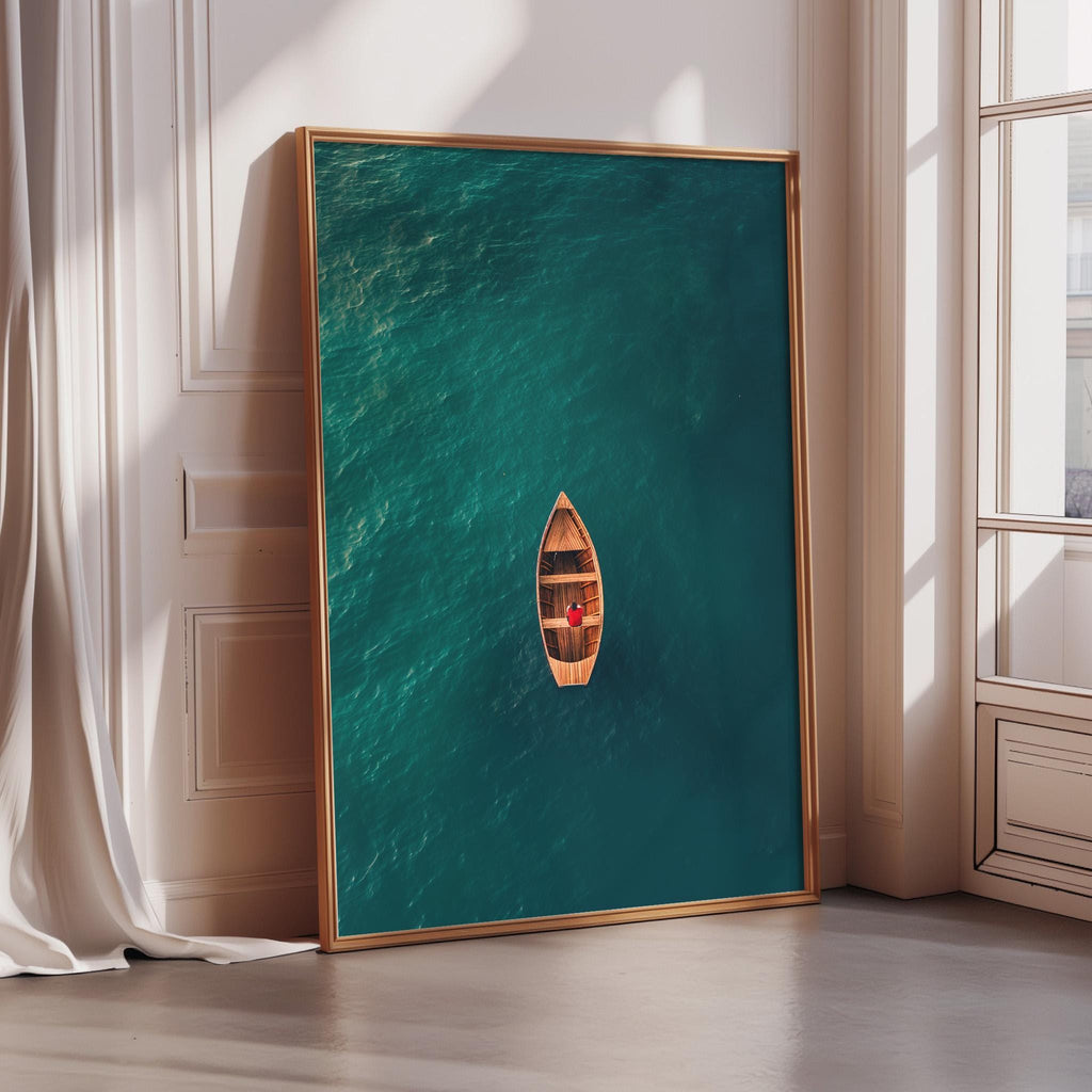 A large framed picture depicting a small wooden boat floating on a turquoise body of water, with a window and white wall in the background.