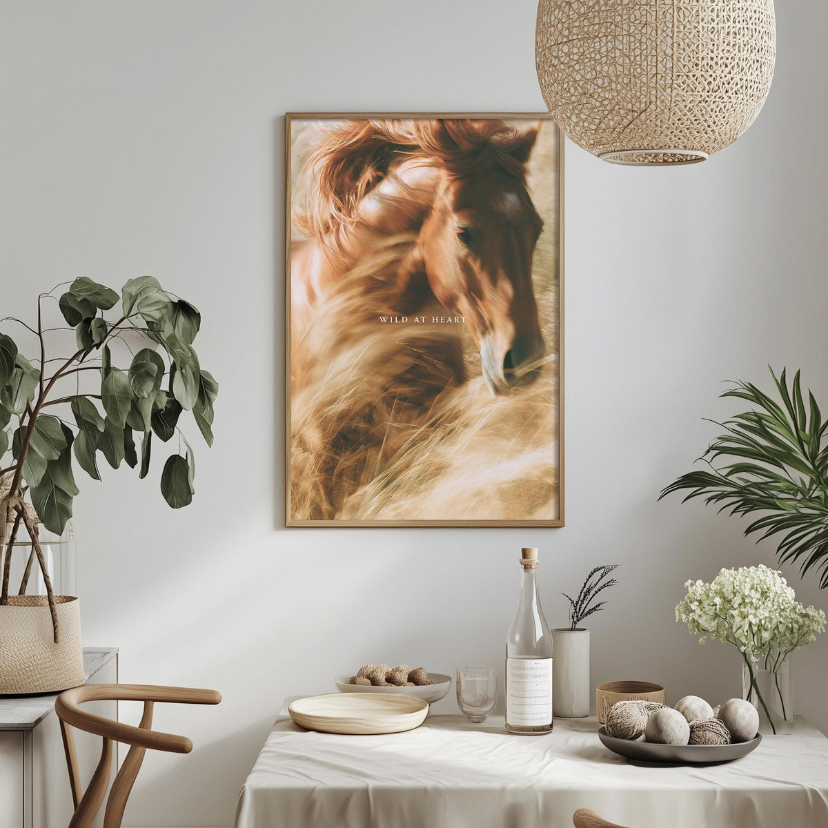 a dining table with a white tablecloth, a bowl of fruit, a bottle, and a vase with flowers. Above the table, there is a framed picture of a horse.