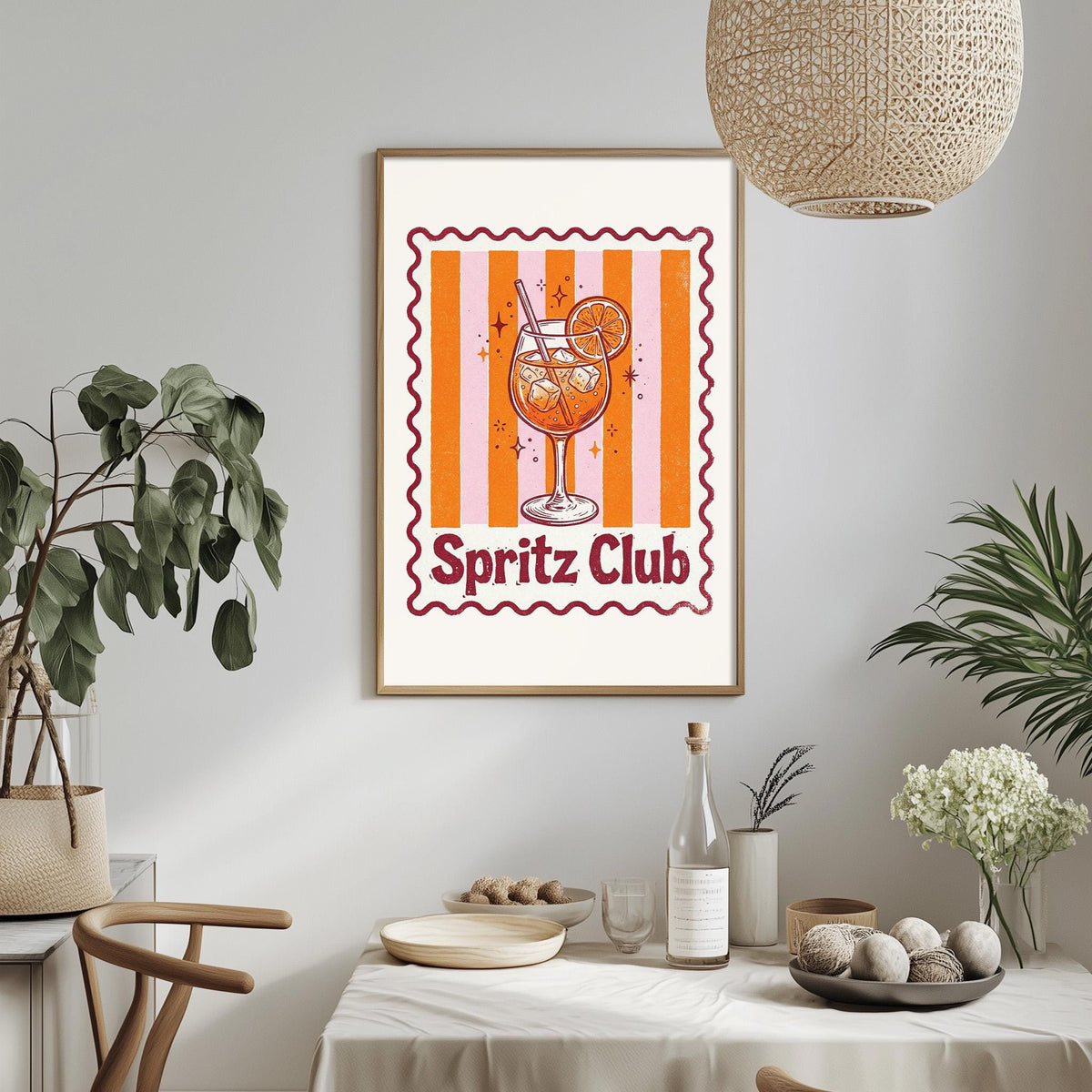 a framed poster of a glass of orange juice with the text "Spritz Club" on it, hanging on a wall above a dining table with various items on it.