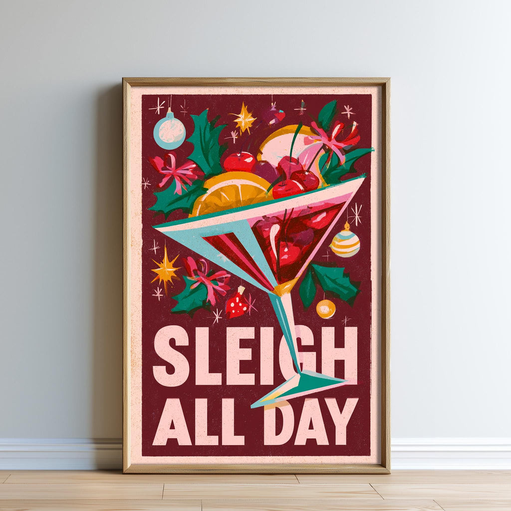 A framed poster with a vibrant design featuring a martini glass filled with various fruits and flowers, surrounded by festive decorations such as stars and ornaments. The text "SLEIGH ALL DAY" is prominently displayed on the poster.