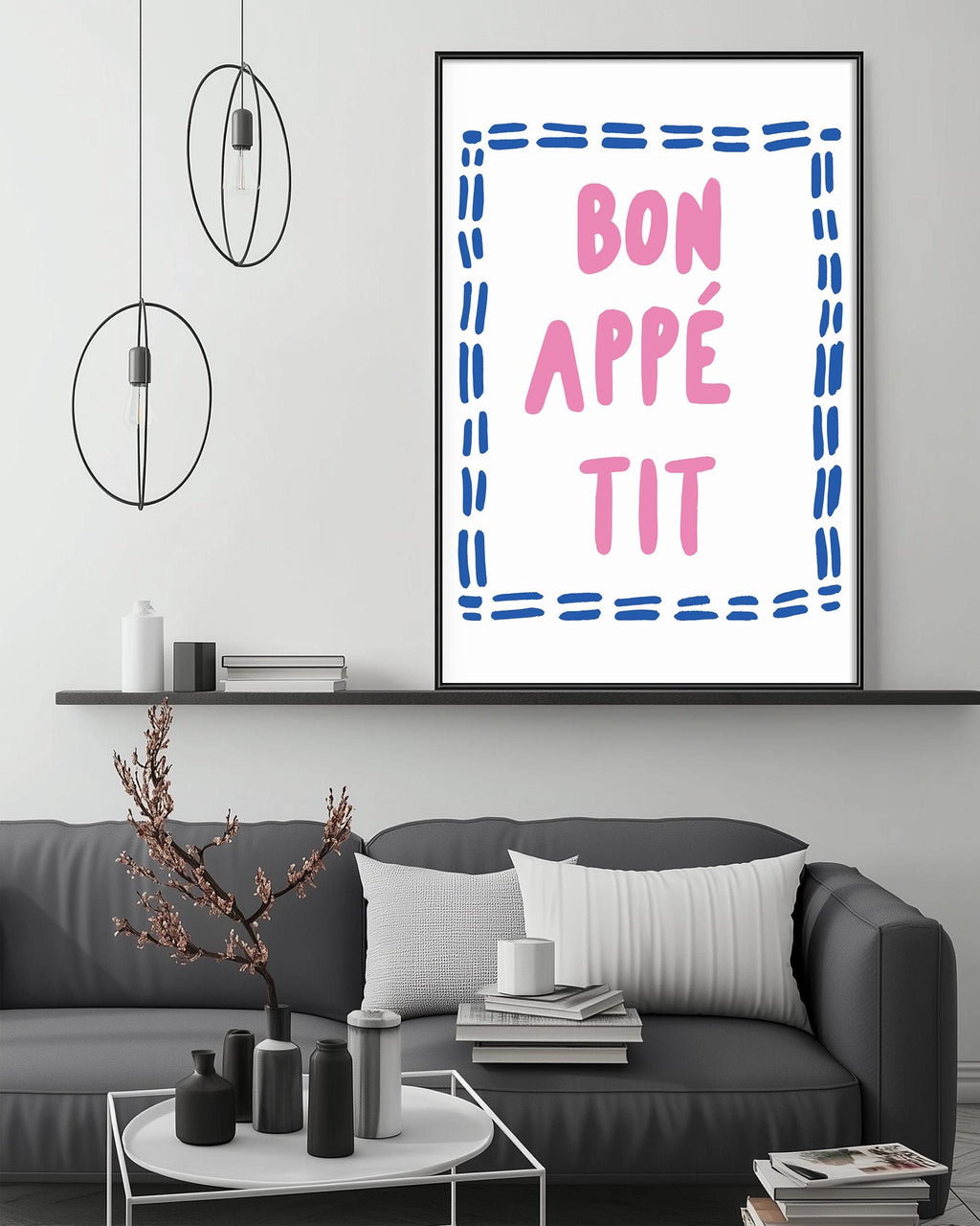 a living room with a gray couch, a coffee table, and a framed poster with the text " bon appe tit" in pink and blue.