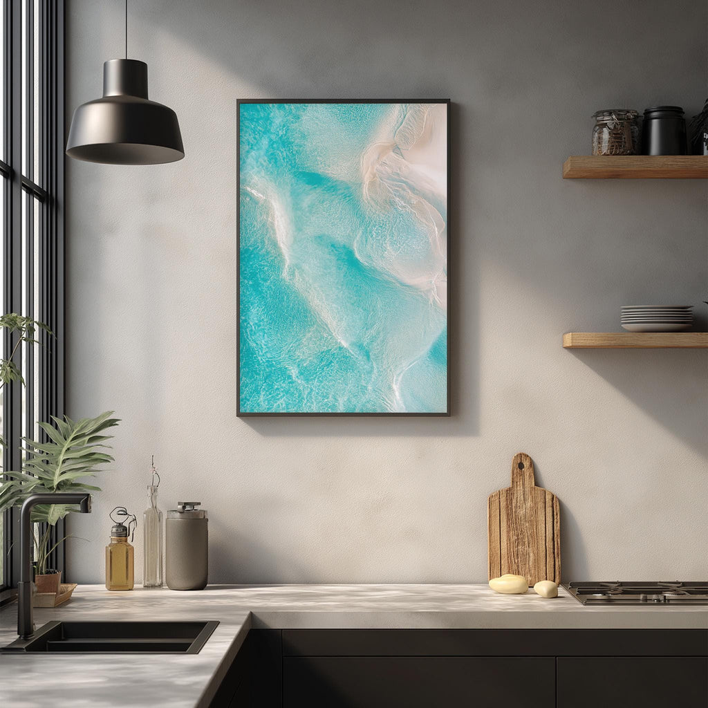 a modern kitchen with a large framed picture of turquoise water hanging on the wall above a wooden cutting board and other kitchen items.