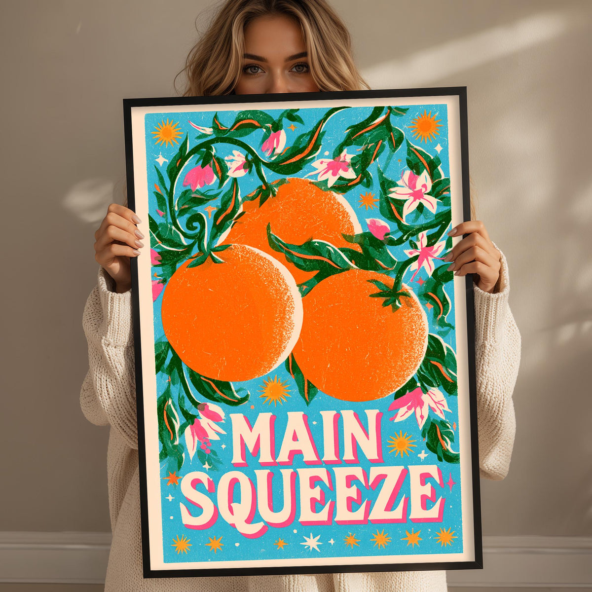 A woman holding a framed poster with a vibrant illustration of oranges and flowers.
