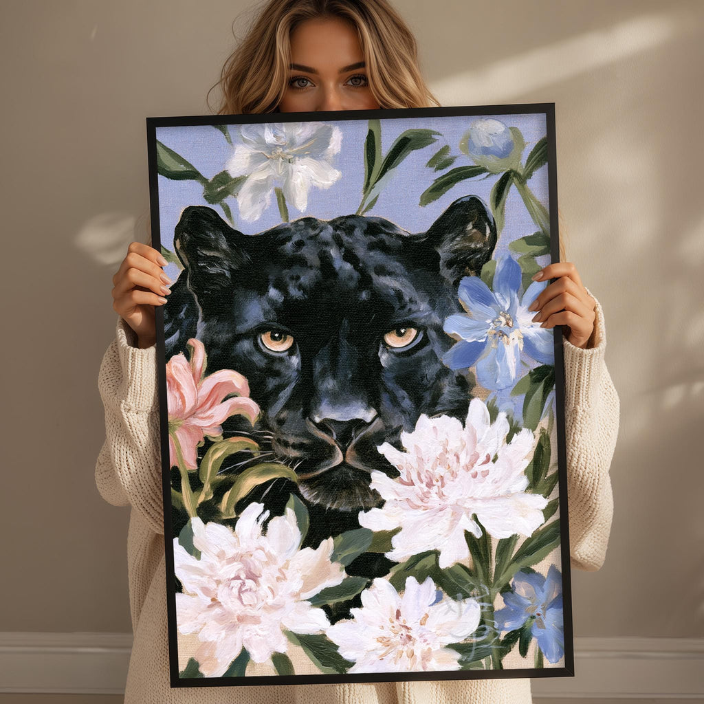 A woman holds up a framed painting of a black panther surrounded by colorful flowers.