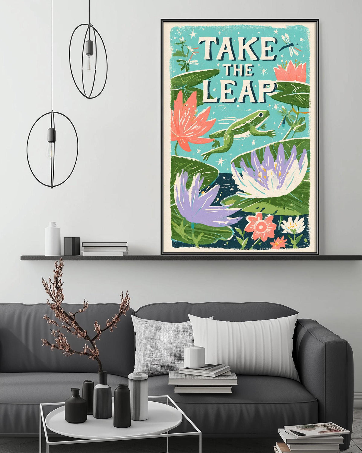 a large framed poster with a vibrant illustration of a frog leaping over a pond filled with colorful flowers, hanging on a wall above a gray couch in a living room setting.