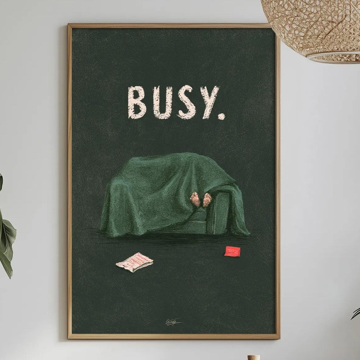 a framed poster with the word "BUSY" on it, hanging on a wall above a dining table with various items on it, such as a bottle, a bowl, and a vase.