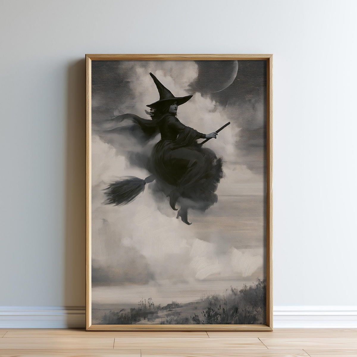 A framed black and white image depicting a witch riding a broomstick against a cloudy sky with a crescent moon.