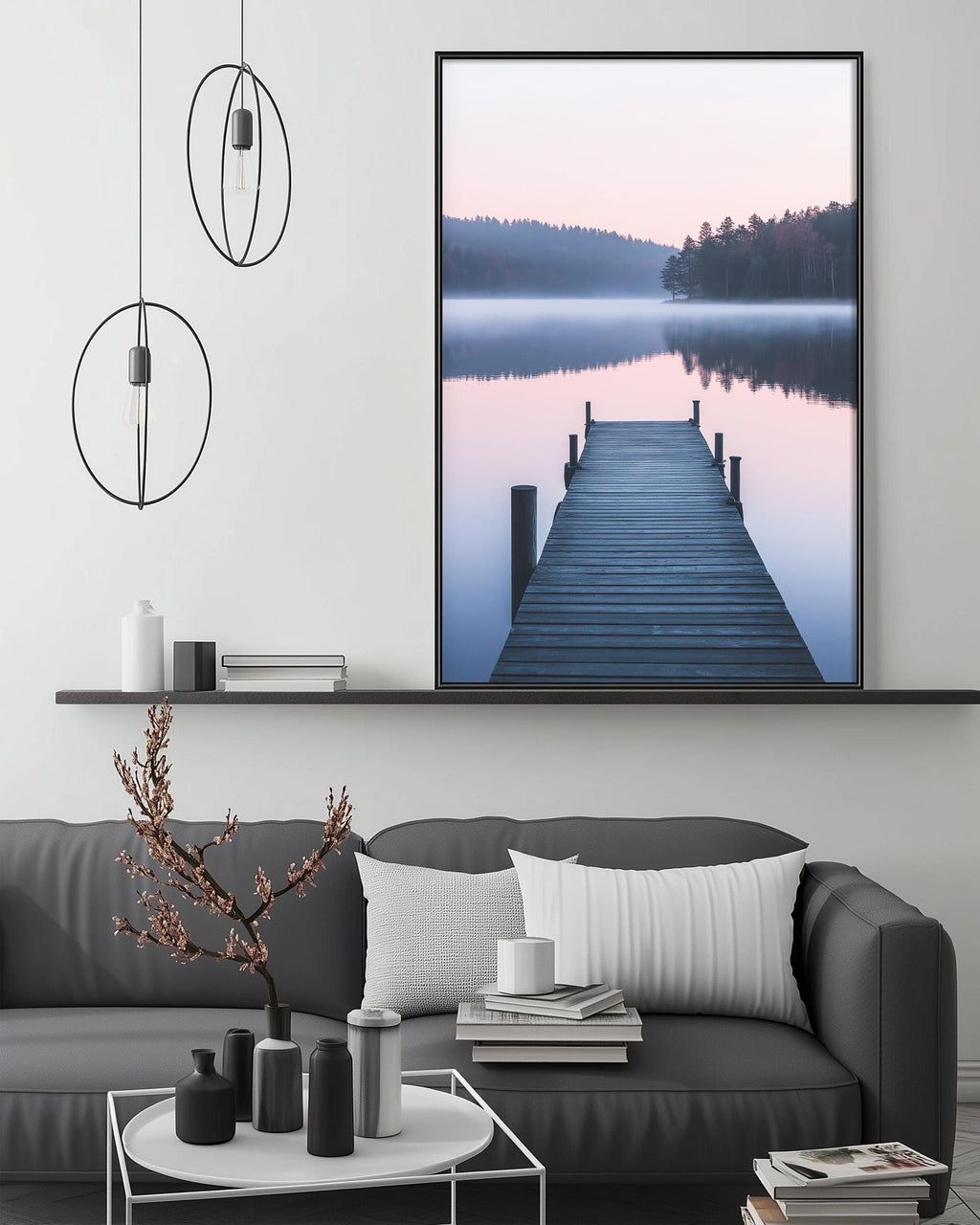 a serene living room with a gray sofa, a coffee table, and a large framed picture of a wooden dock leading to a calm lake. The room has a minimalist and modern design, with a black and white color scheme and a few decorative elements such as a potted plant and a vase.