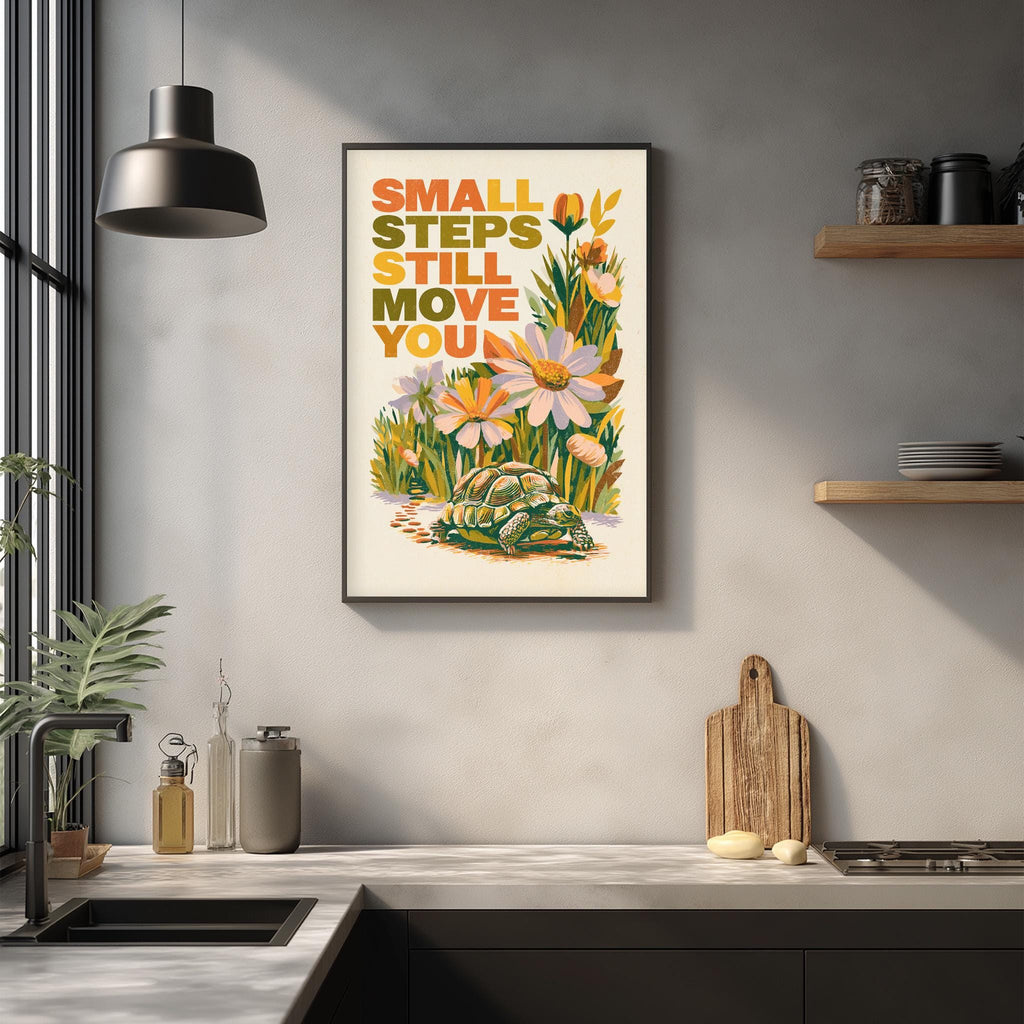 a framed poster with the text "Small steps still move you" displayed on a wall above a kitchen counter with various kitchen items such as a cutting board, bottles, and a sink.