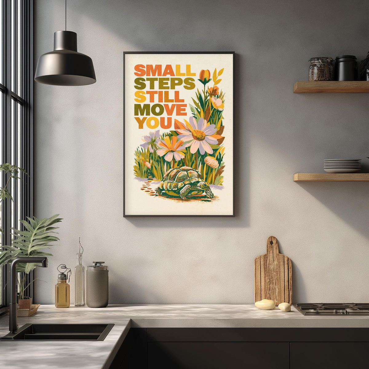 a framed poster with the text "Small steps still move you" displayed on a wall above a kitchen counter with various kitchen items such as a cutting board, bottles, and a sink.