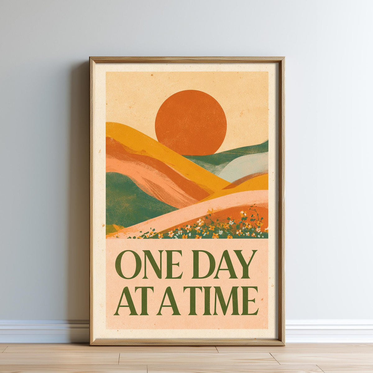The image is a framed poster with a landscape scene featuring mountains, hills, and a large sun in the sky. The text on the poster reads "ONE DAY AT A TIME".