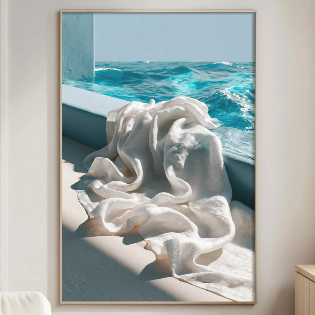 a large framed picture of a white towel hanging on a wall, with a view of the ocean through a window.