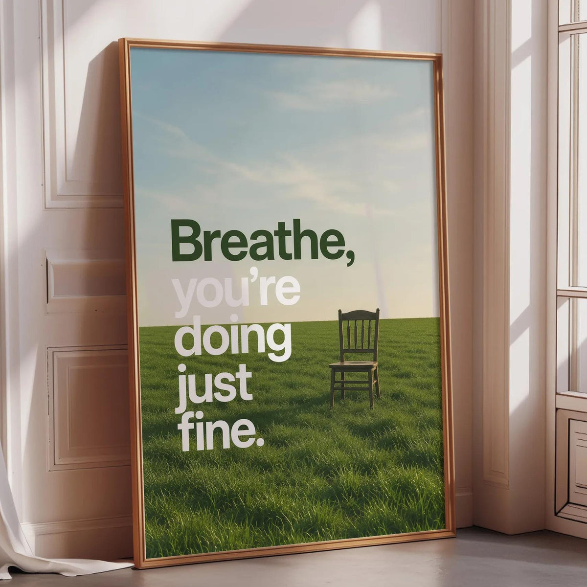 a large framed poster with a serene landscape of a grassy field and a solitary chair, accompanied by the text "Breathe, you're doing just fine."