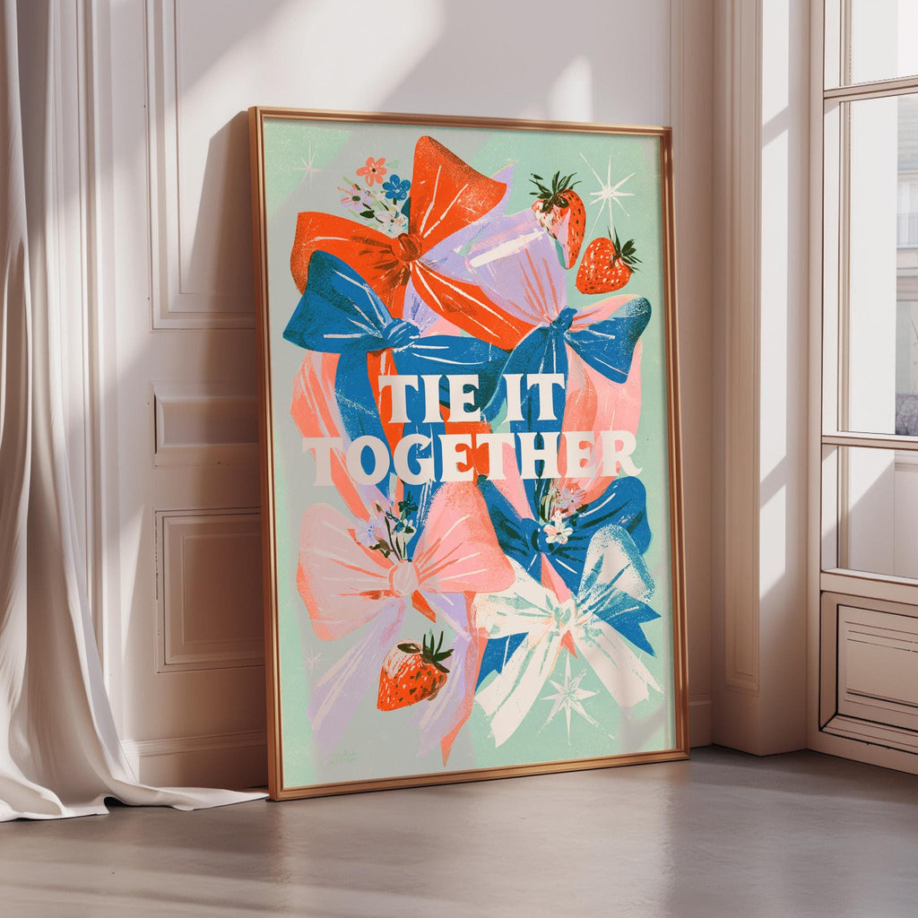 a large framed poster with a colorful illustration of bows and strawberries. The poster has the text "tie it together" written on it.
