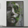a modern living room with a gray sofa, a coffee table, and a large framed artwork depicting a stone face with green moss growing on it. The room has a minimalist and contemporary design, with a black and white color scheme.