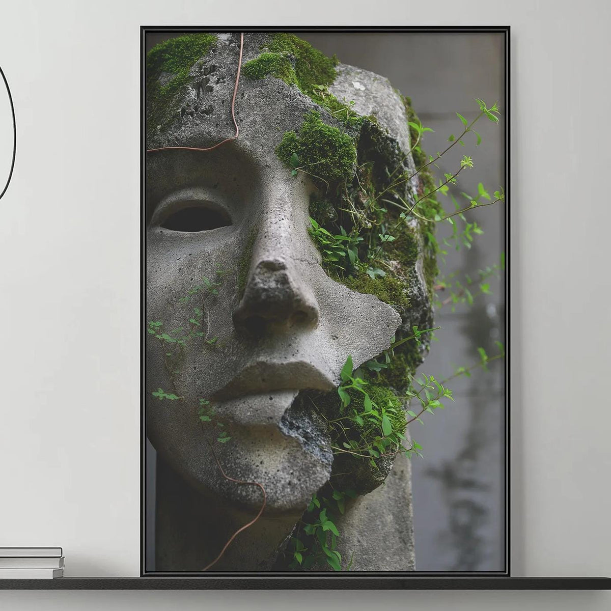 a modern living room with a gray sofa, a coffee table, and a large framed artwork depicting a stone face with green moss growing on it. The room has a minimalist and contemporary design, with a black and white color scheme.