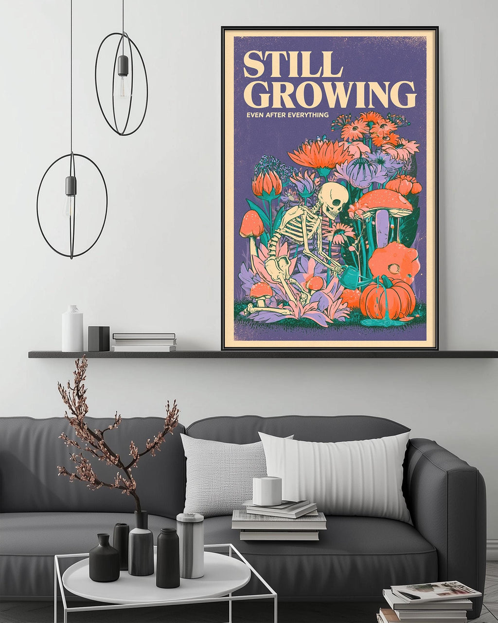 a poster of a skeleton surrounded by flowers and mushrooms, hanging on a wall above a gray couch with a coffee table in front of it.