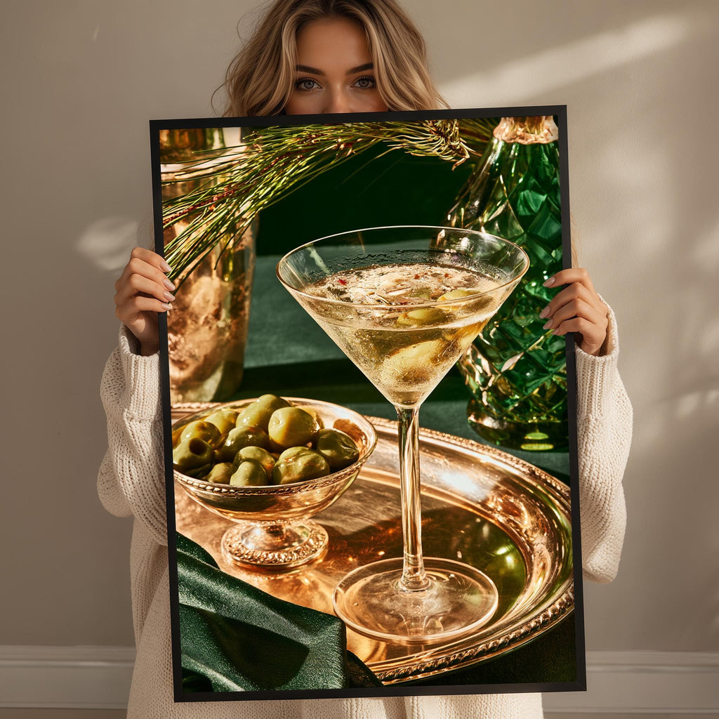 A woman holds up a framed photograph of a martini glass filled with a drink, surrounded by a bowl of olives and a green vase.