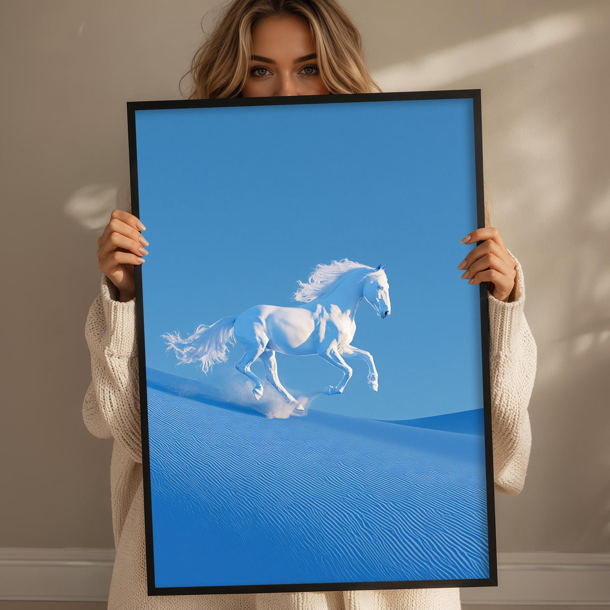 A woman holds up a framed image of a white horse galloping across a sandy landscape against a blue sky.