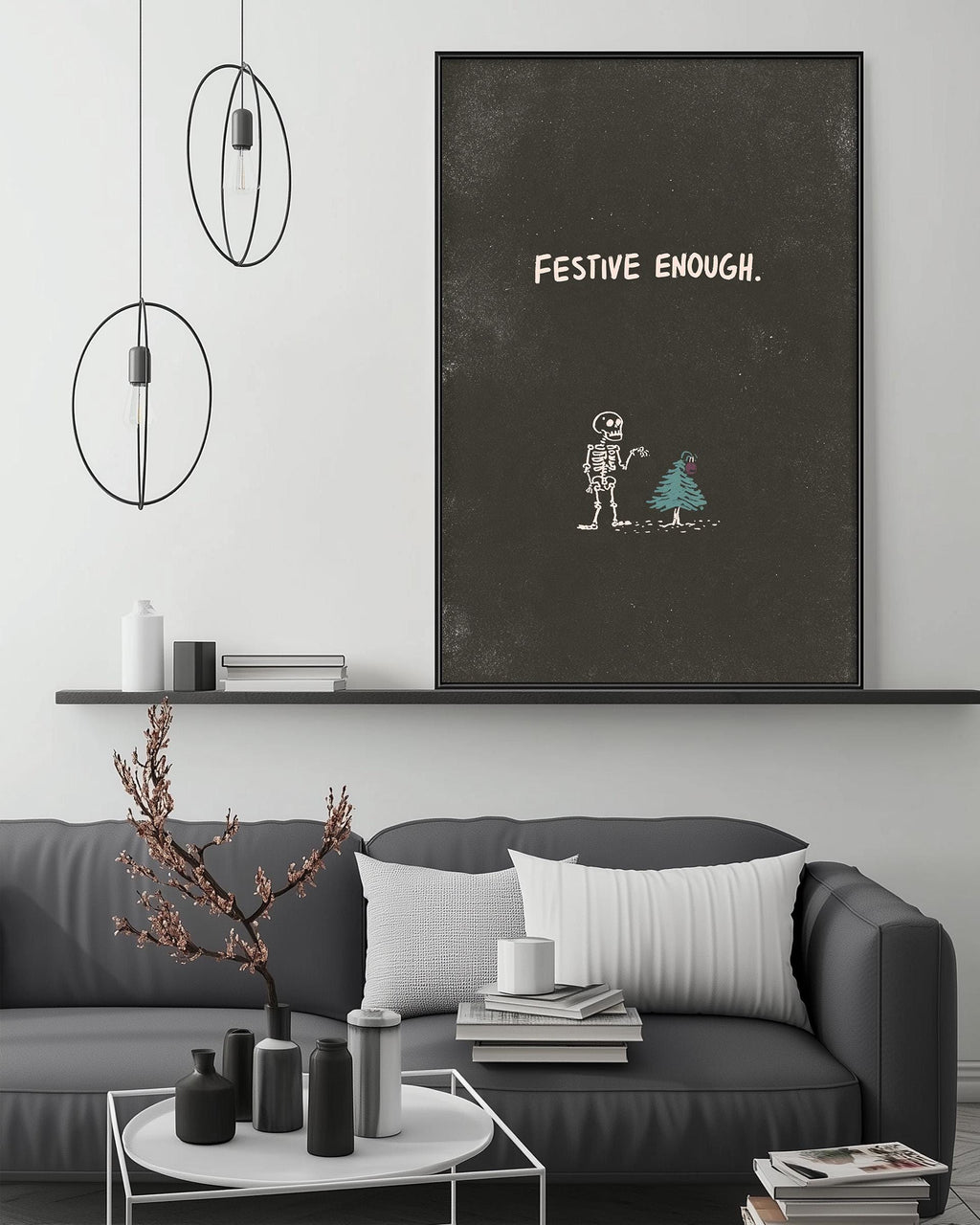 a living room with a gray sofa, a coffee table, and a large black and white poster on the wall. The poster has a skeleton and a Christmas tree drawn on it, along with the text "FESTIVE ENOUGH."