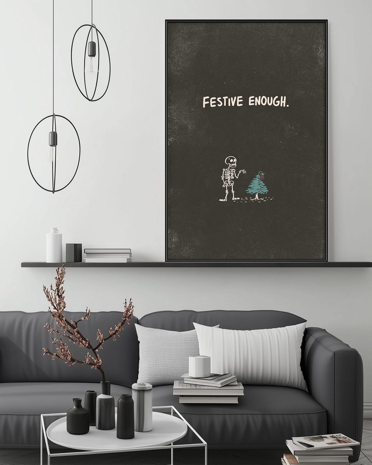 a living room with a gray sofa, a coffee table, and a large black and white poster on the wall. The poster has a skeleton and a Christmas tree drawn on it, along with the text "FESTIVE ENOUGH."