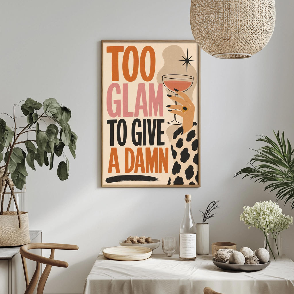 a framed poster with the text "Too Glam to Give a Damn" displayed on a wall above a dining table with various items on it.
