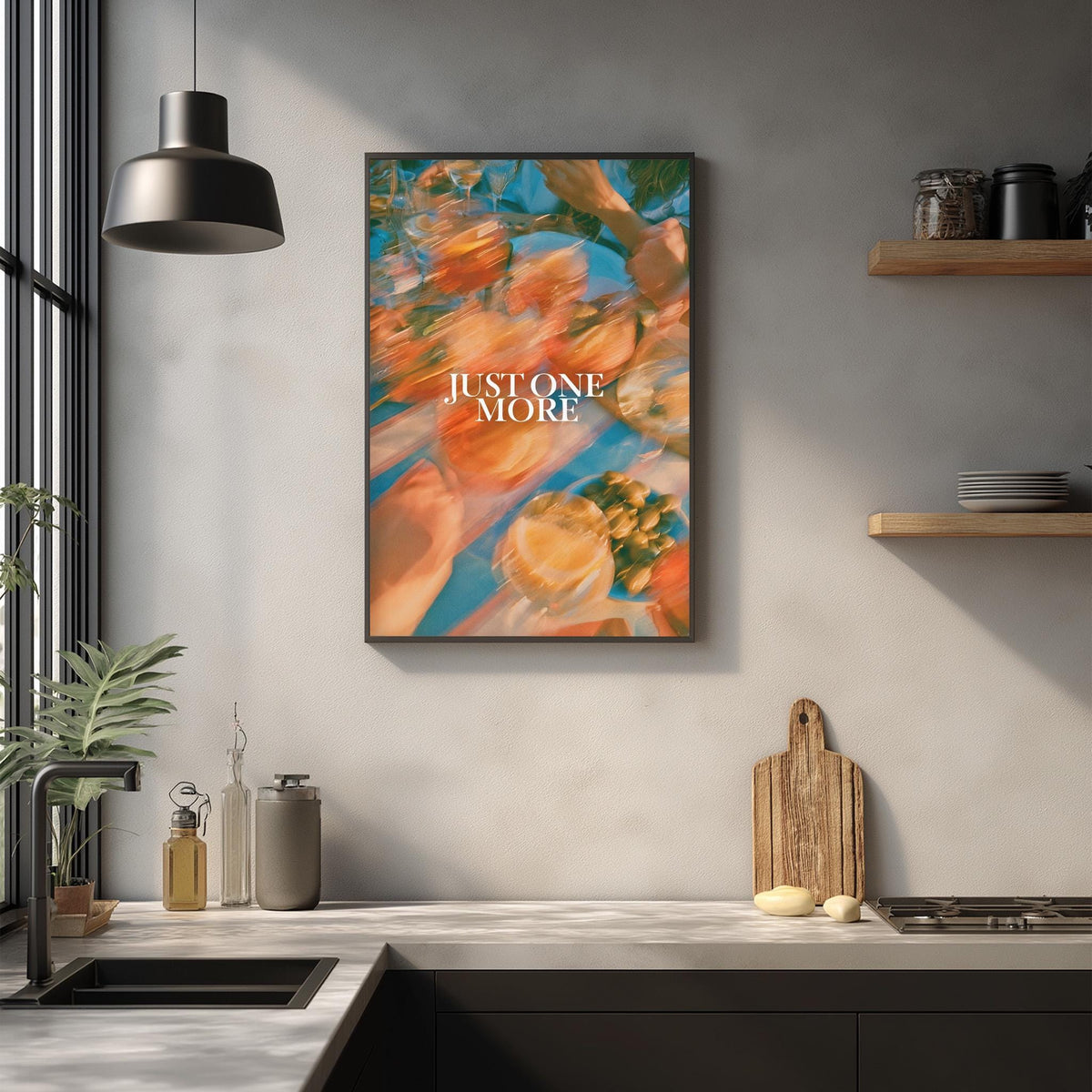 a kitchen counter with various items such as a cutting board, a bottle, and a plant. Above the counter, there is a framed poster with the text "JUSTONE MORE" displayed on it.