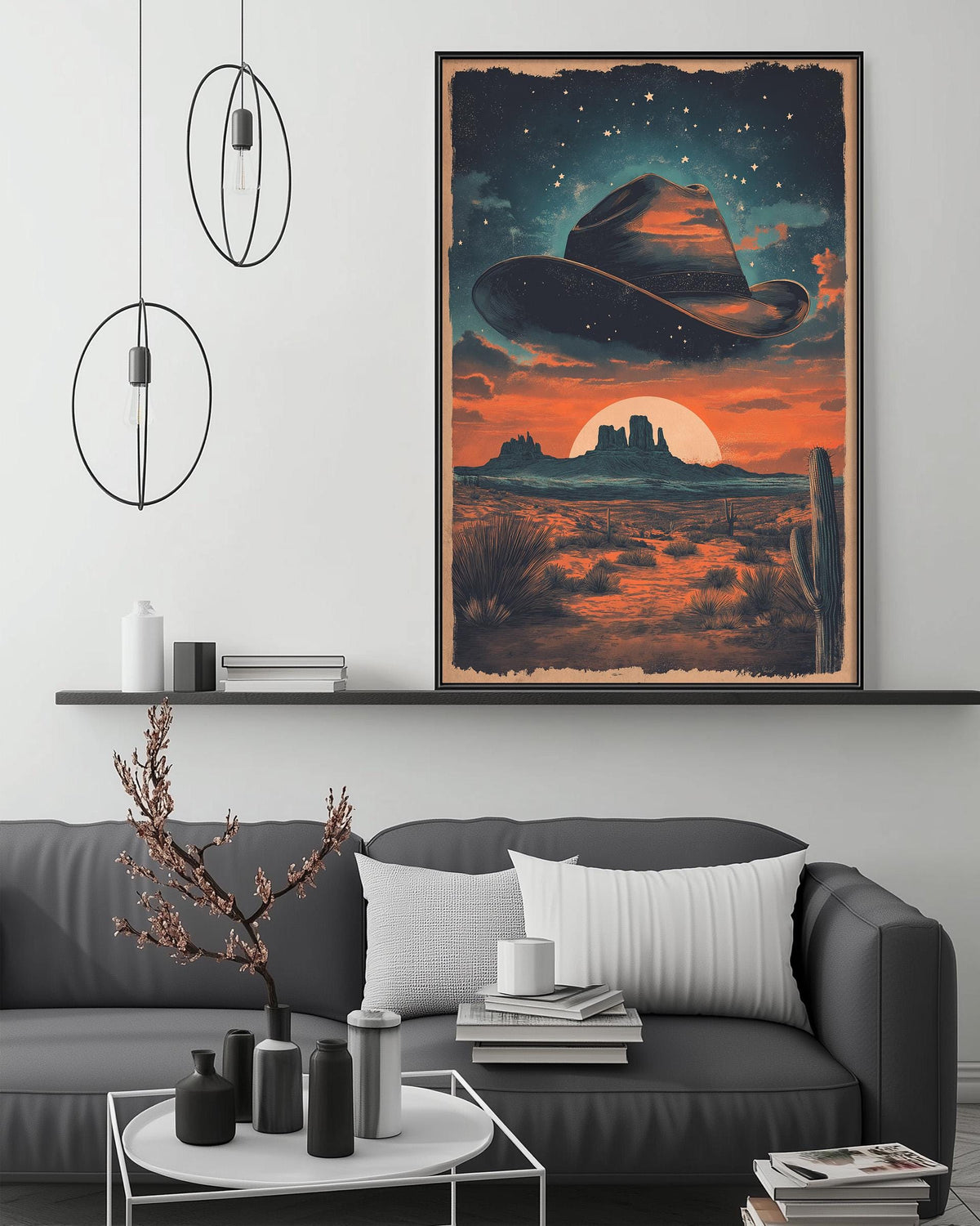 a large framed poster of a desert landscape with a cowboy hat in the sky, hanging on a wall above a gray couch with a coffee table in front of it.
