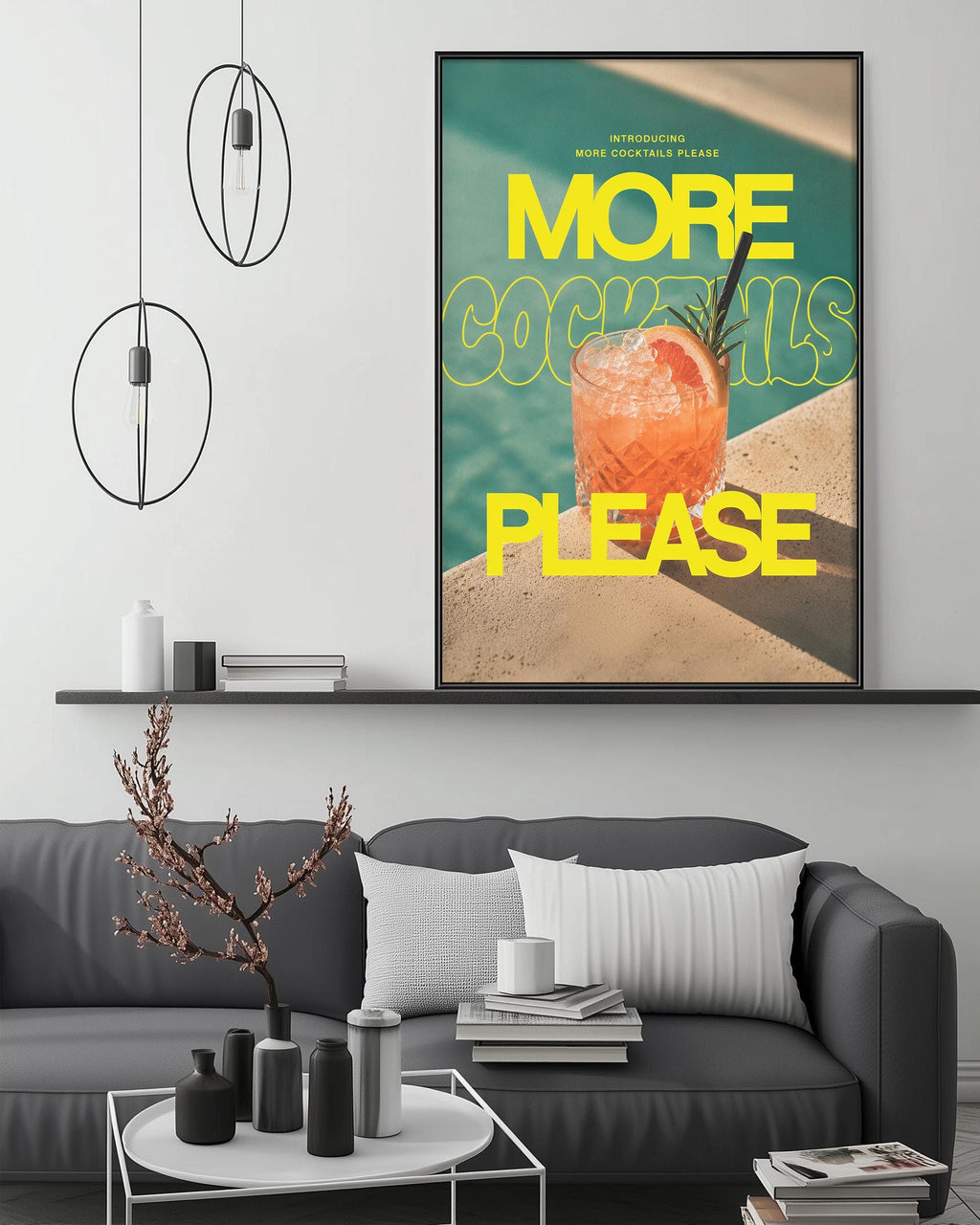 a living room with a gray couch, a coffee table, and a large framed poster on the wall. The poster has a vibrant design with a cocktail glass and the text "MORE COCKTAILS PLEASE" in bold yellow and black letters.