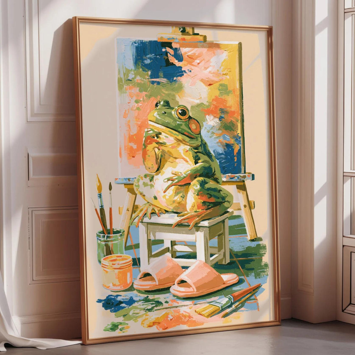 A framed painting depicting a frog sitting on a chair surrounded by art supplies, including paintbrushes and a palette, in an indoor setting.