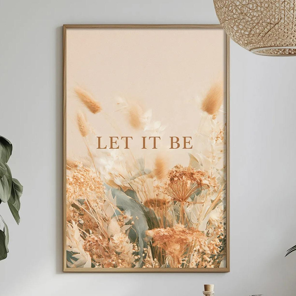 a dining table with a bowl of fruit, a bottle, and a vase of flowers, along with a framed poster with the text "LET IT BE" hanging on the wall above the table.