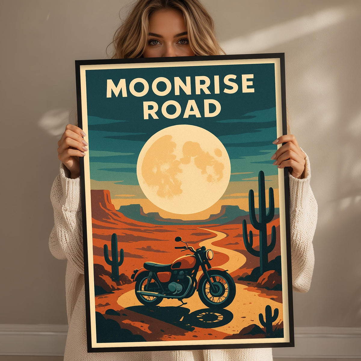 A woman holds up a framed poster depicting a desert landscape with a cactus, a motorcycle, and a large moon in the sky.