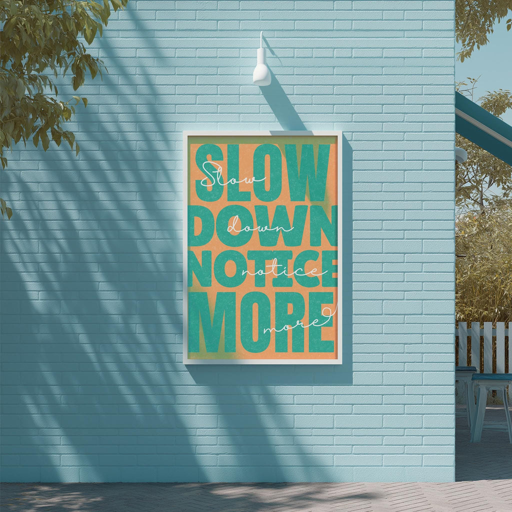 a poster with the text "SLOW DOWN NOTICE MORE" displayed on a blue brick wall.