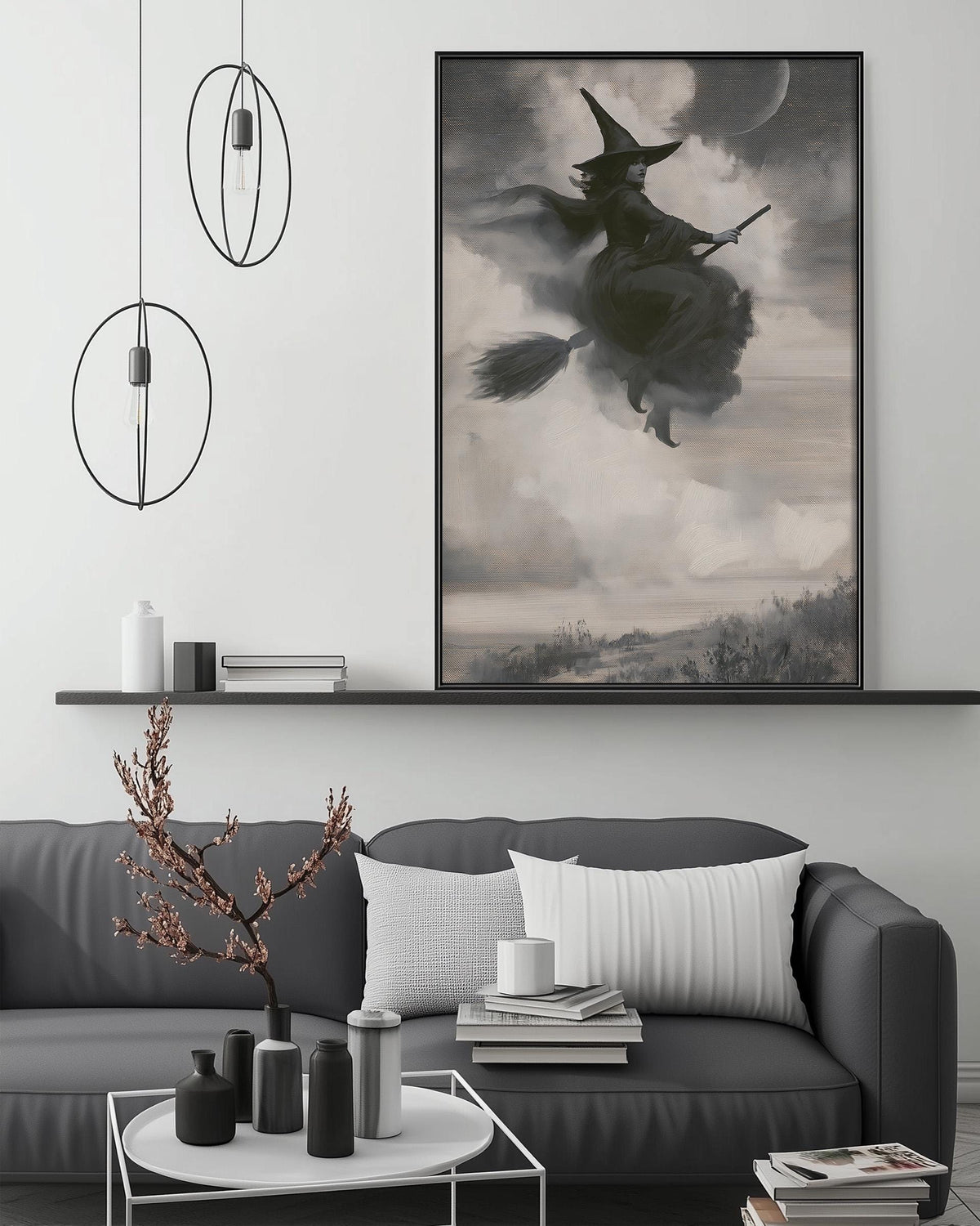 a large black and white painting of a witch on a broomstick, hanging on a wall above a gray couch with white pillows. The painting is surrounded by various decorative items, such as a potted plant, vases, and books, creating a cozy and stylish living room setting.